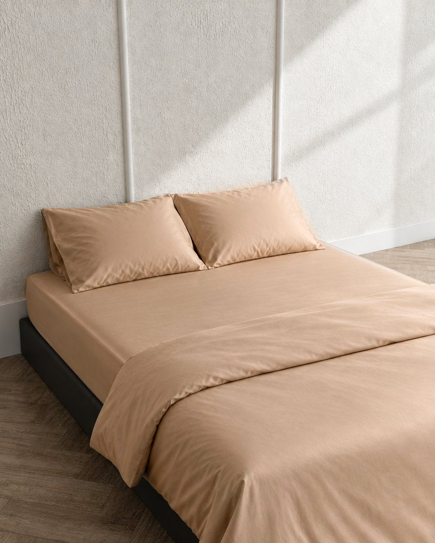 Light beige silky cotton sateen fitted sheet and pillowcases on a low bed, seen from above
