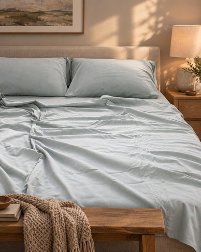 Pale blue plain cotton flat sheet and pillows, styled in a cosy contemporary bedroom