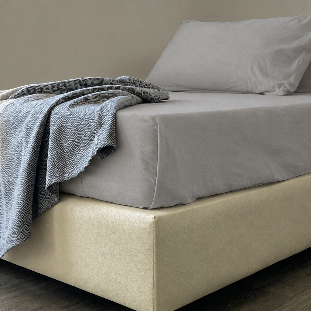Light Grey plain cotton flat sheet and pillowcase on a mattress with a blue knitted throw.
