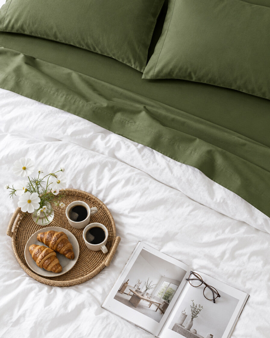 Olive green plain cotton flat sheet seen from above with a breakfast tray of coffee and croissants