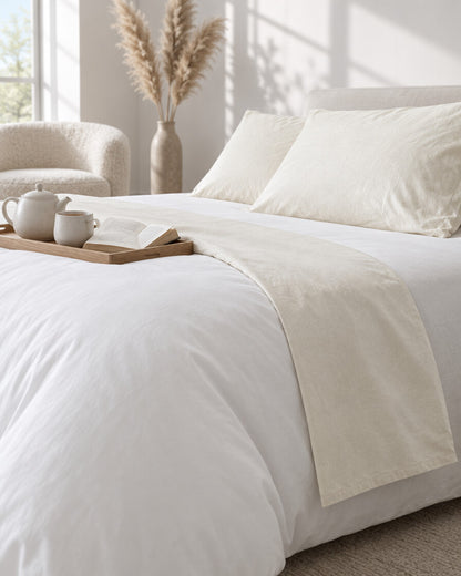 Cream plain cotton flat sheet with a tea tray and open book, a boucle armchair in the corner