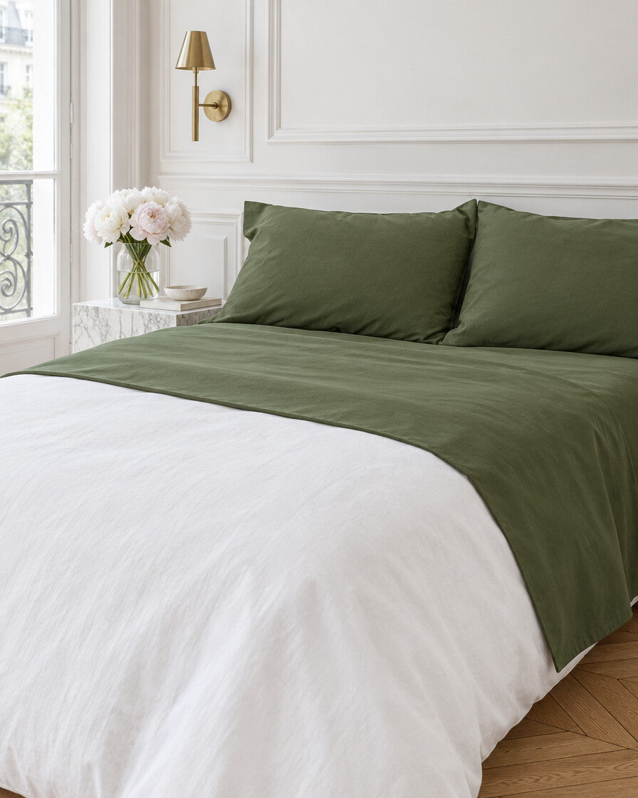 Olive green plain cotton flat sheet in a Parisian bedroom with panelled walls and fresh peonies