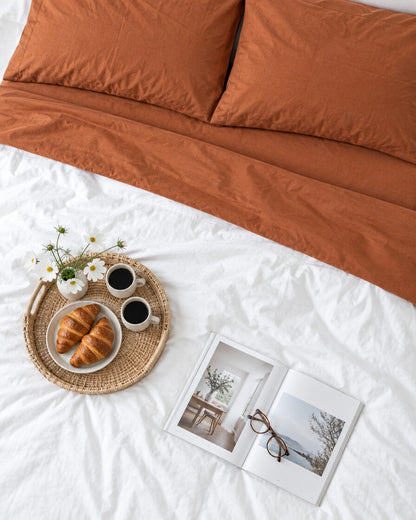 Terracotta plain cotton flat sheet seen from above with a breakfast tray of coffee and croissants