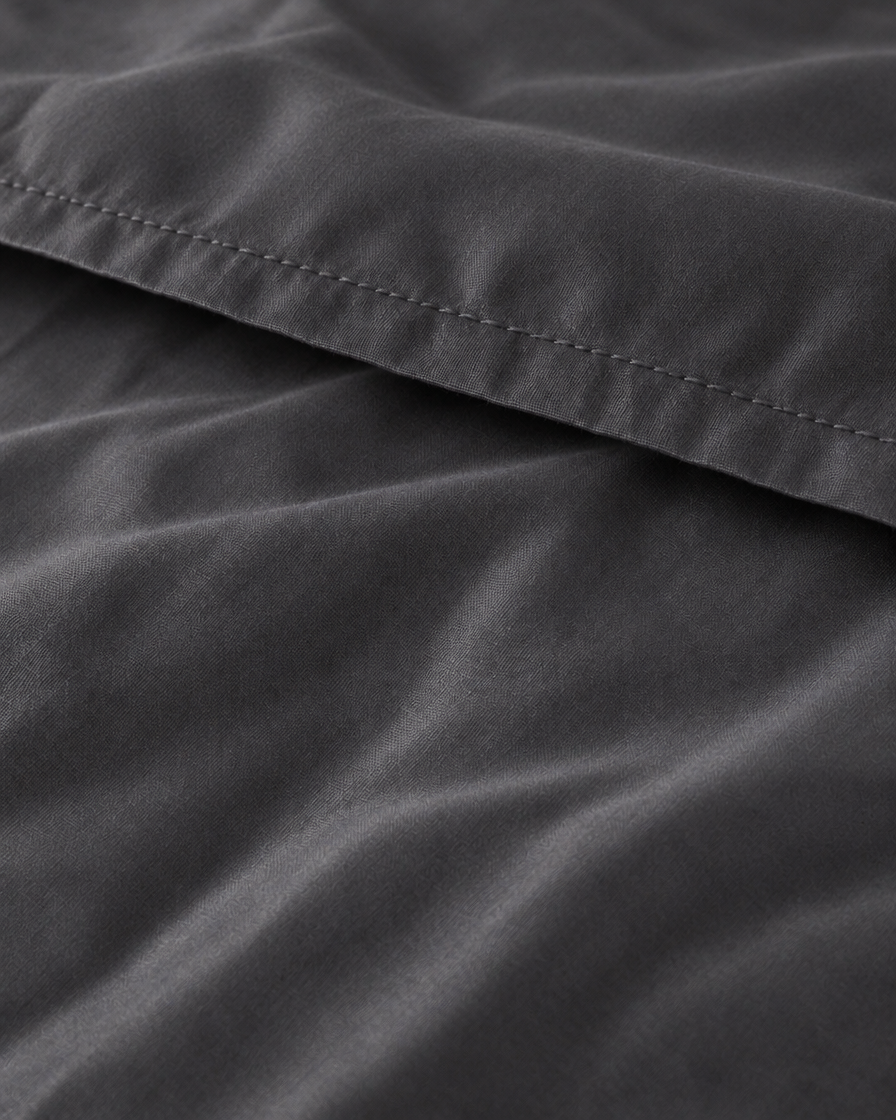 Macro of the stitched hem on a Charcoal Grey silky cotton flat sheet, showing the grey sateen sheen.