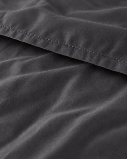 Macro of the stitched hem on a Charcoal Grey silky cotton flat sheet, showing the grey sateen sheen.