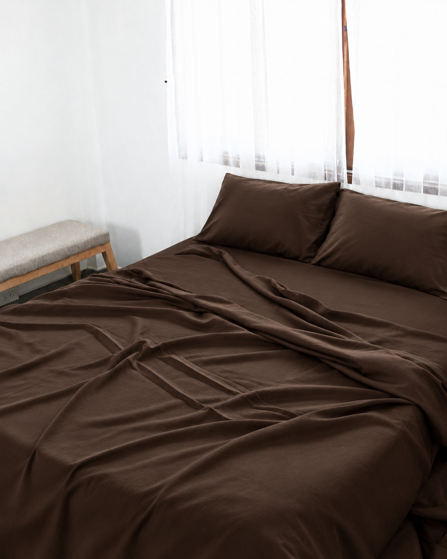 Chocolate silky cotton flat sheet, a chocolate brown cotton sateen flat sheet, with matching pillowcases on a bed beside a bright window.