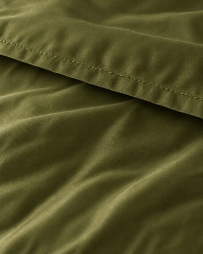 Macro of the stitched hem on a Juniper Green silky cotton flat sheet, showing the olive green sateen sheen.
