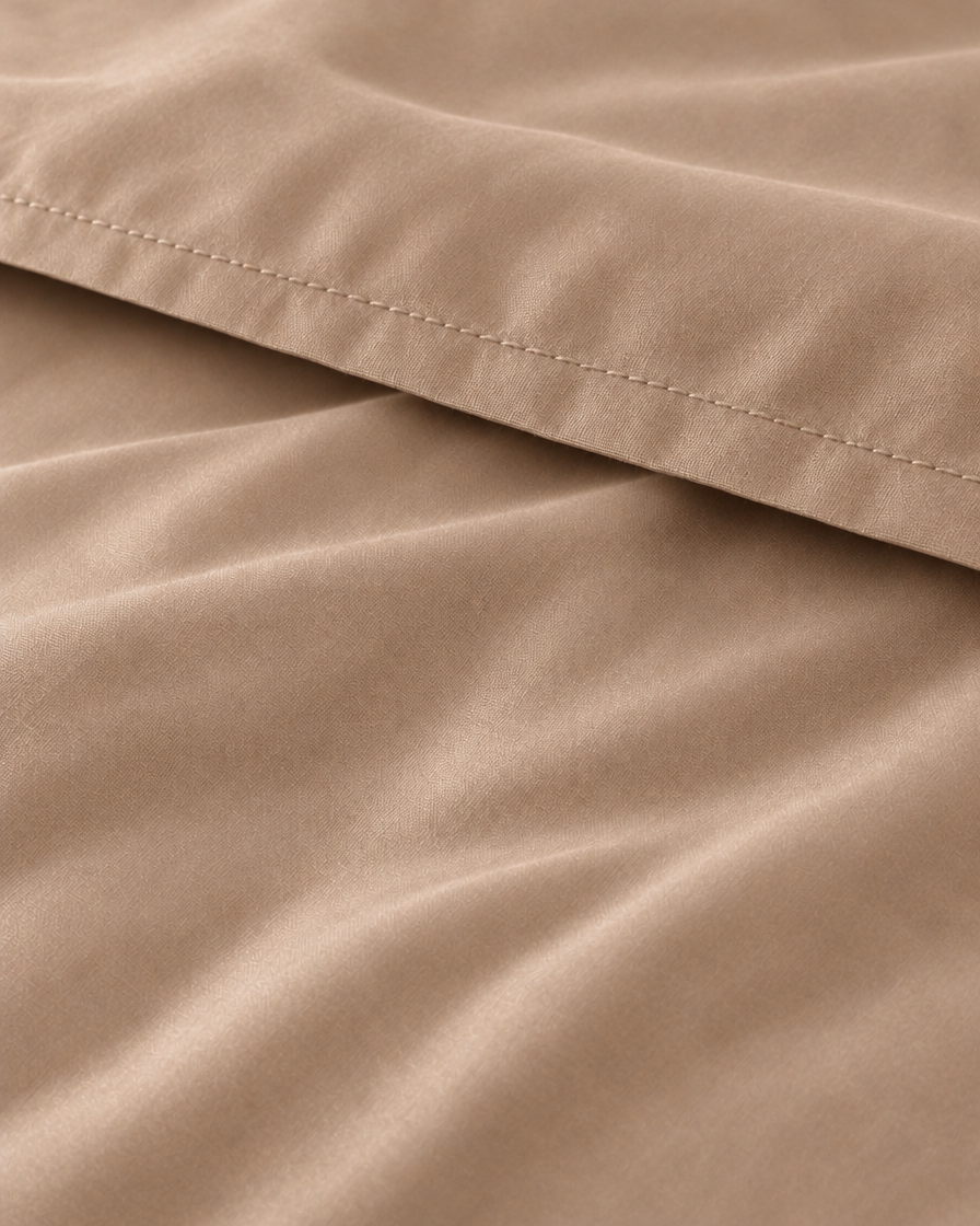 Macro of the stitched hem on a Light Beige silky cotton flat sheet, showing the beige sateen sheen.