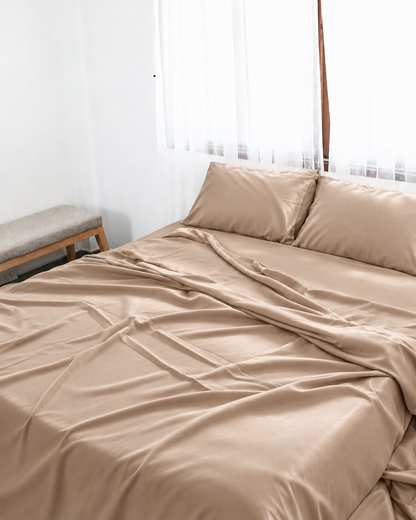 Light Beige silky cotton flat sheet, a beige cotton sateen flat sheet, with matching pillowcases on a bed beside a bright window.