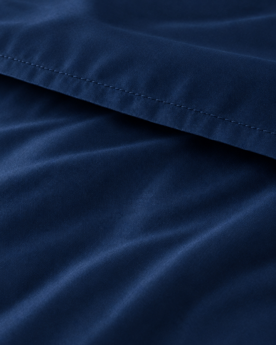 Macro of the stitched hem on a Marine Blue silky cotton flat sheet, showing the navy blue sateen sheen.