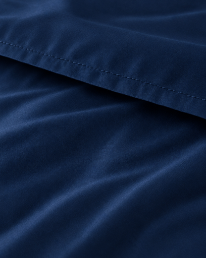 Macro of the stitched hem on a Marine Blue silky cotton flat sheet, showing the navy blue sateen sheen.