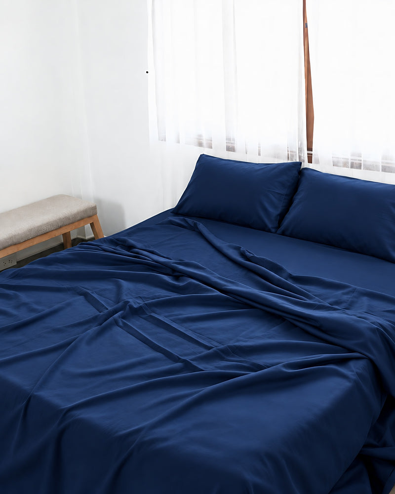 Marine Blue silky cotton flat sheet, a navy blue cotton sateen flat sheet, with matching pillowcases on a bed beside a bright window