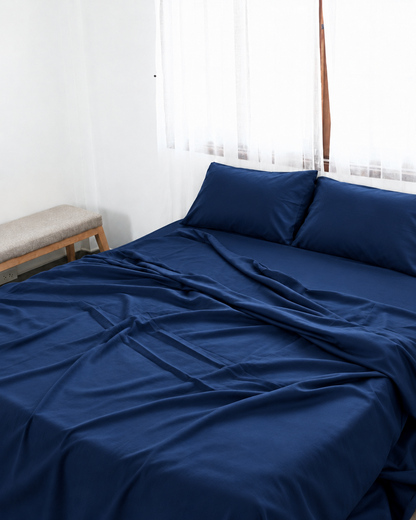 Marine Blue silky cotton flat sheet, a navy blue cotton sateen flat sheet, with matching pillowcases on a bed beside a bright window.