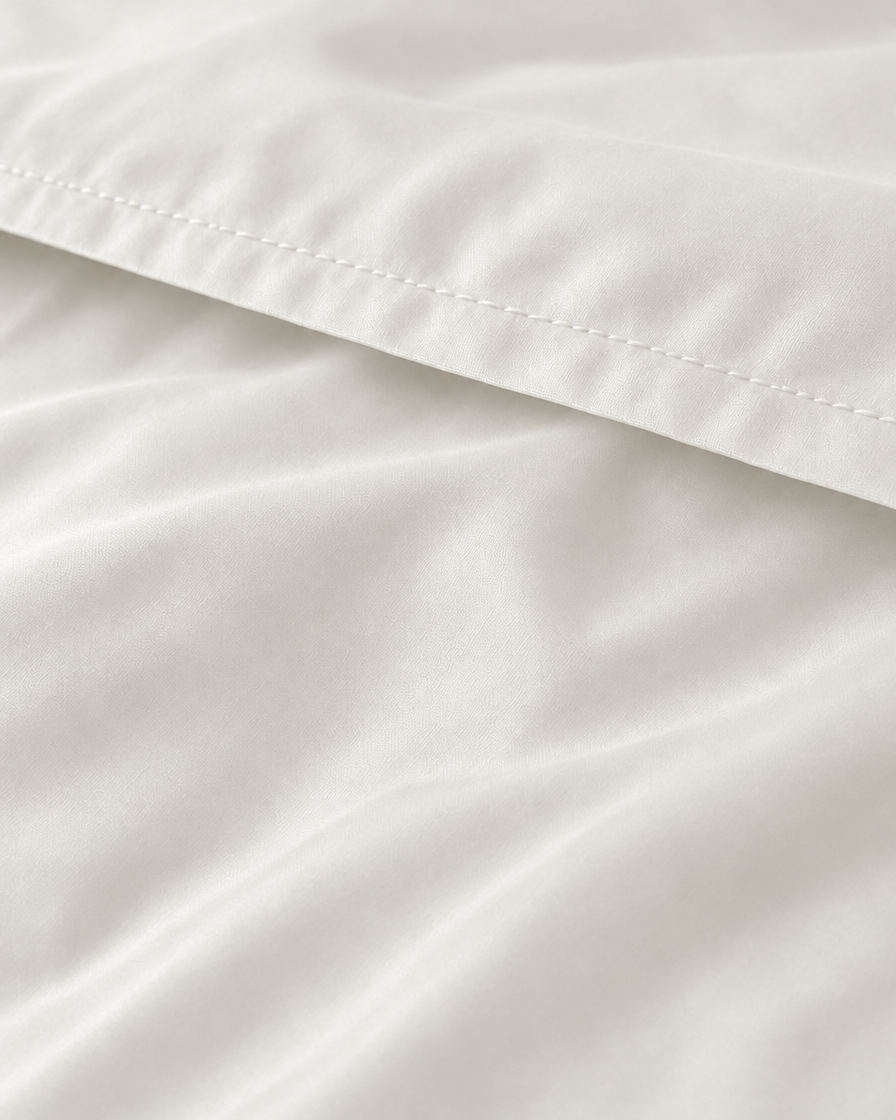 Macro of the stitched hem on a Milky White silky cotton flat sheet, showing the white sateen sheen.