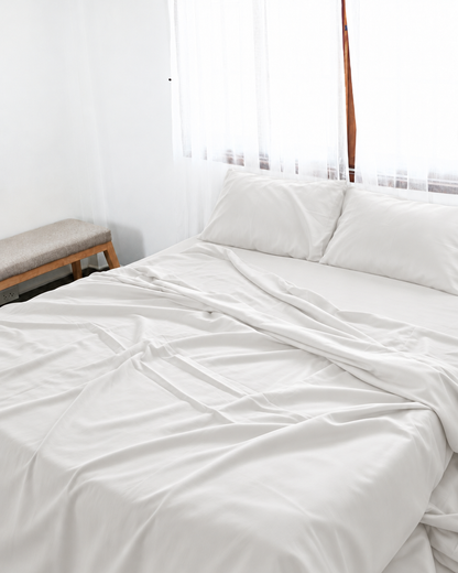 Milky White silky cotton flat sheet, a white cotton sateen flat sheet, with matching pillowcases on a bed beside a bright window.