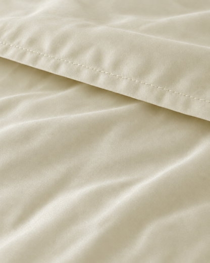 Macro of the stitched hem on a Vanilla silky cotton flat sheet, showing the cream sateen sheen.