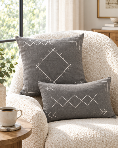 Grey cushions with ivory diamond and arrow stitching on a bouclé armchair by a window with a coffee cup