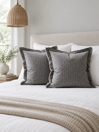 Grey pinstripe flanged cushions on a white bed with an oatmeal knit throw folded at the foot