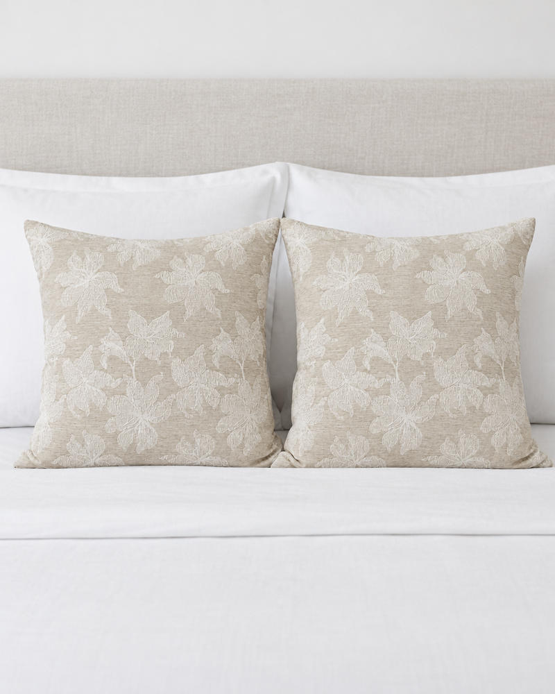 Two Cream Lily Jacquard Cotton cushion covers propped against white pillows on a made bed