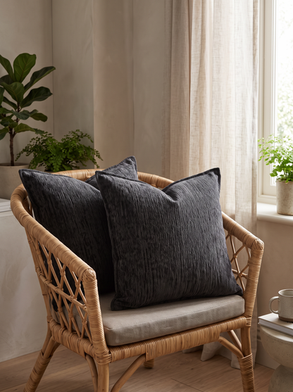 Heathered Jacquard Cushion Covers in Charcoal, styled at home on a rattan armchair by a window