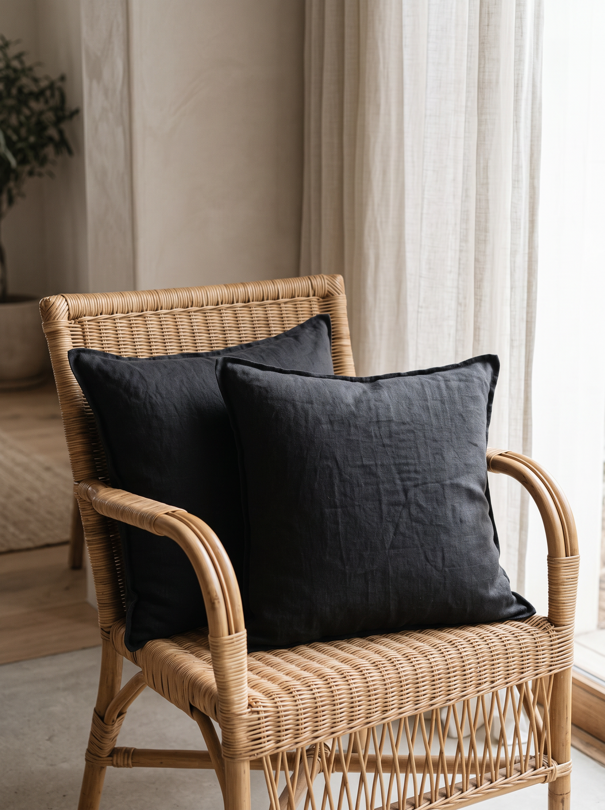 Enzyme-Washed Linen Cotton Cushion Covers in Black, styled at home on a rattan armchair by a window