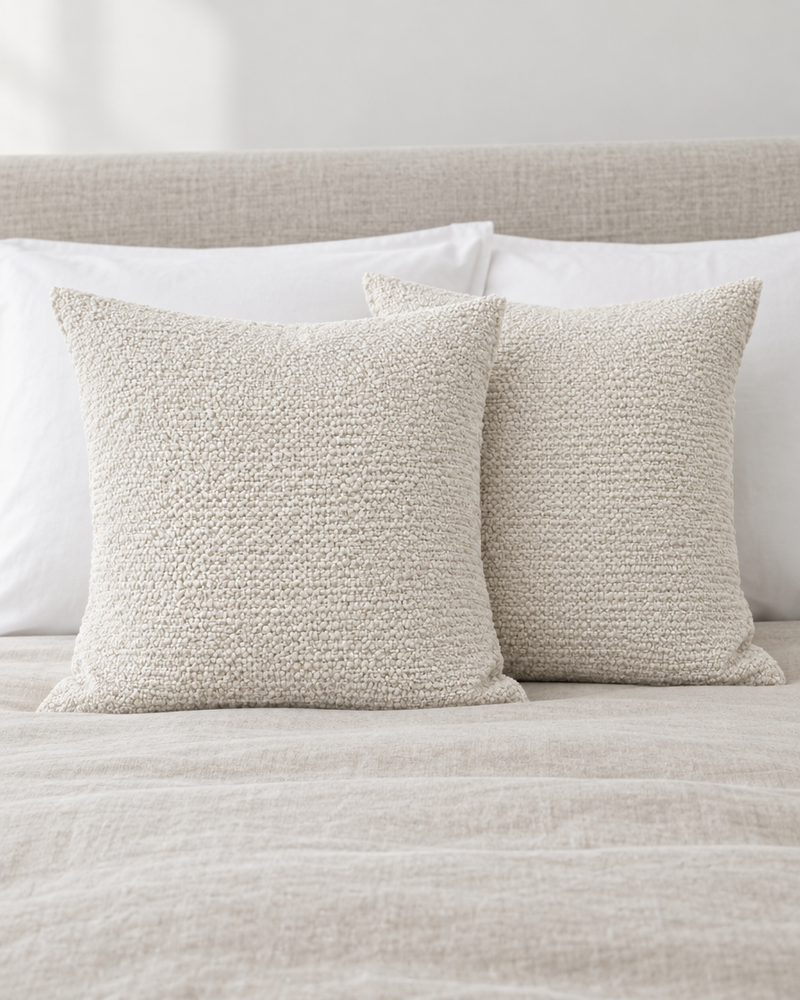 Two ivory textured jacquard cotton linen cushion covers propped against white pillows on a made bed