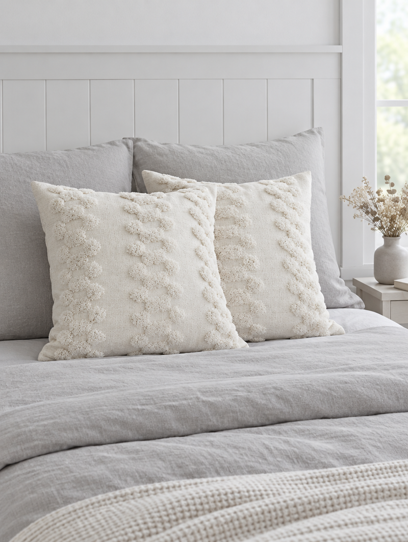 Ivory cloud-embroidered cushions on soft grey linen bedding against a white panelled wall