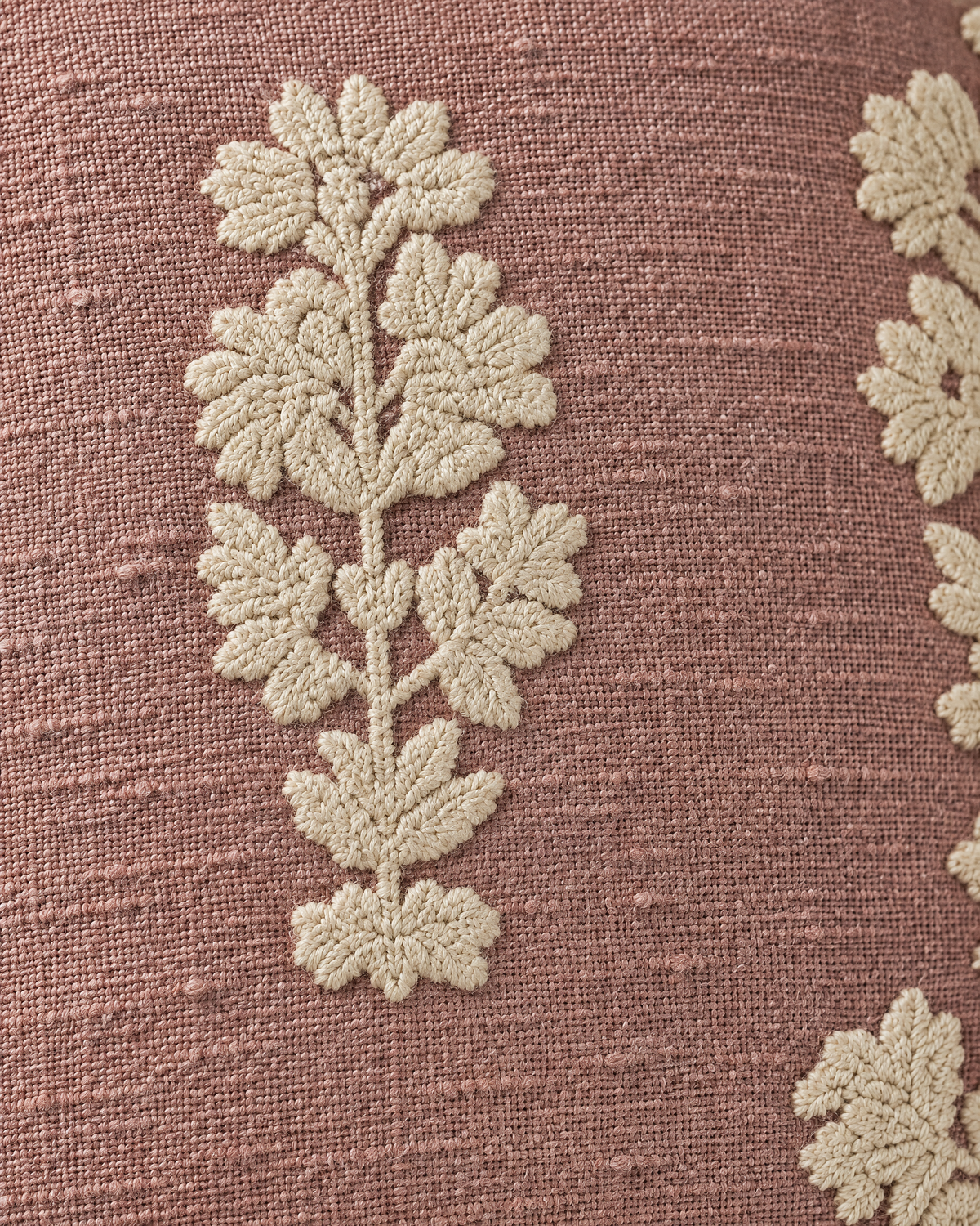 Macro close-up of an ivory crewel-style flower spray raised above the slubbed dusty-rose weave