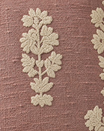 Macro close-up of an ivory crewel-style flower spray raised above the slubbed dusty-rose weave