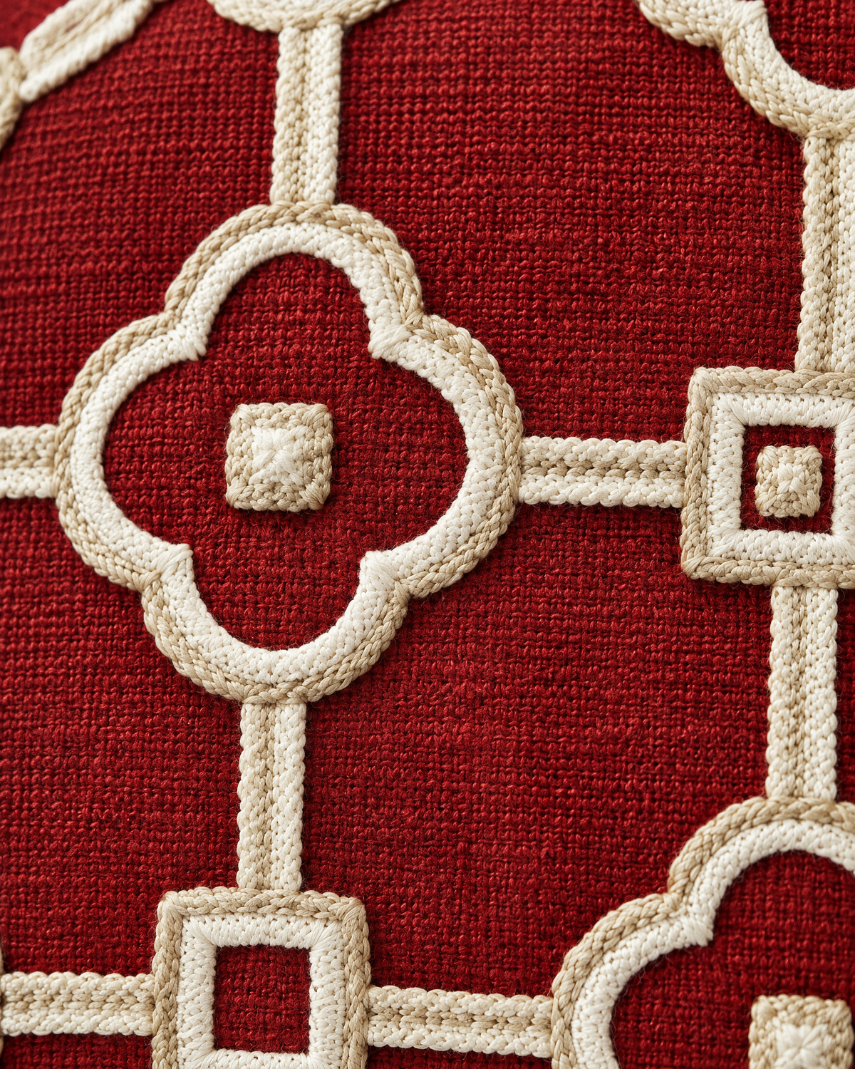 Macro close-up of the ivory chain-stitch quatrefoil lattice with a knotted square centre on brick-red ramie