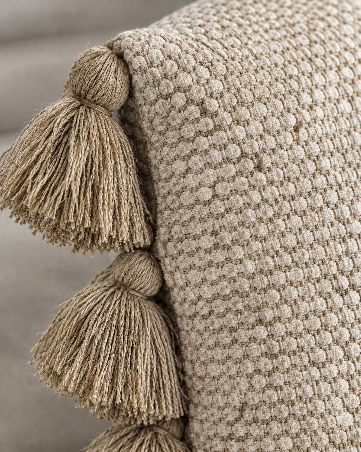 Macro close-up of the oat raised honeycomb weave with two chunky knotted khaki tassels along the side seam