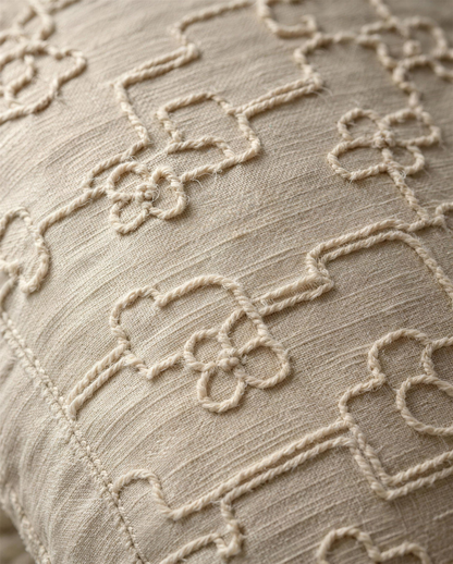 Macro close-up of the oat cord embroidery, a soft raised cord couched in a lattice of stepped lines and four-petal flowers on slubbed oat cloth