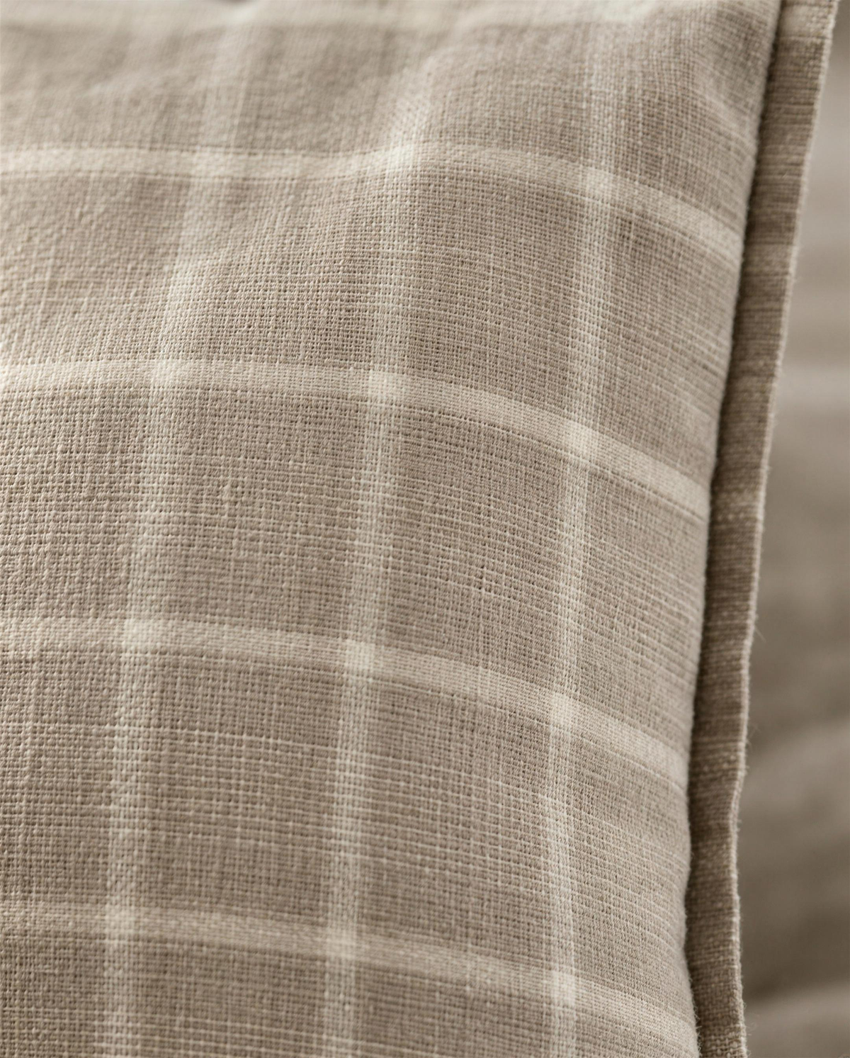 Macro close-up of the Taupe Check printed linen, the open linen weave showing through the soft taupe and ivory check beside the flange edge