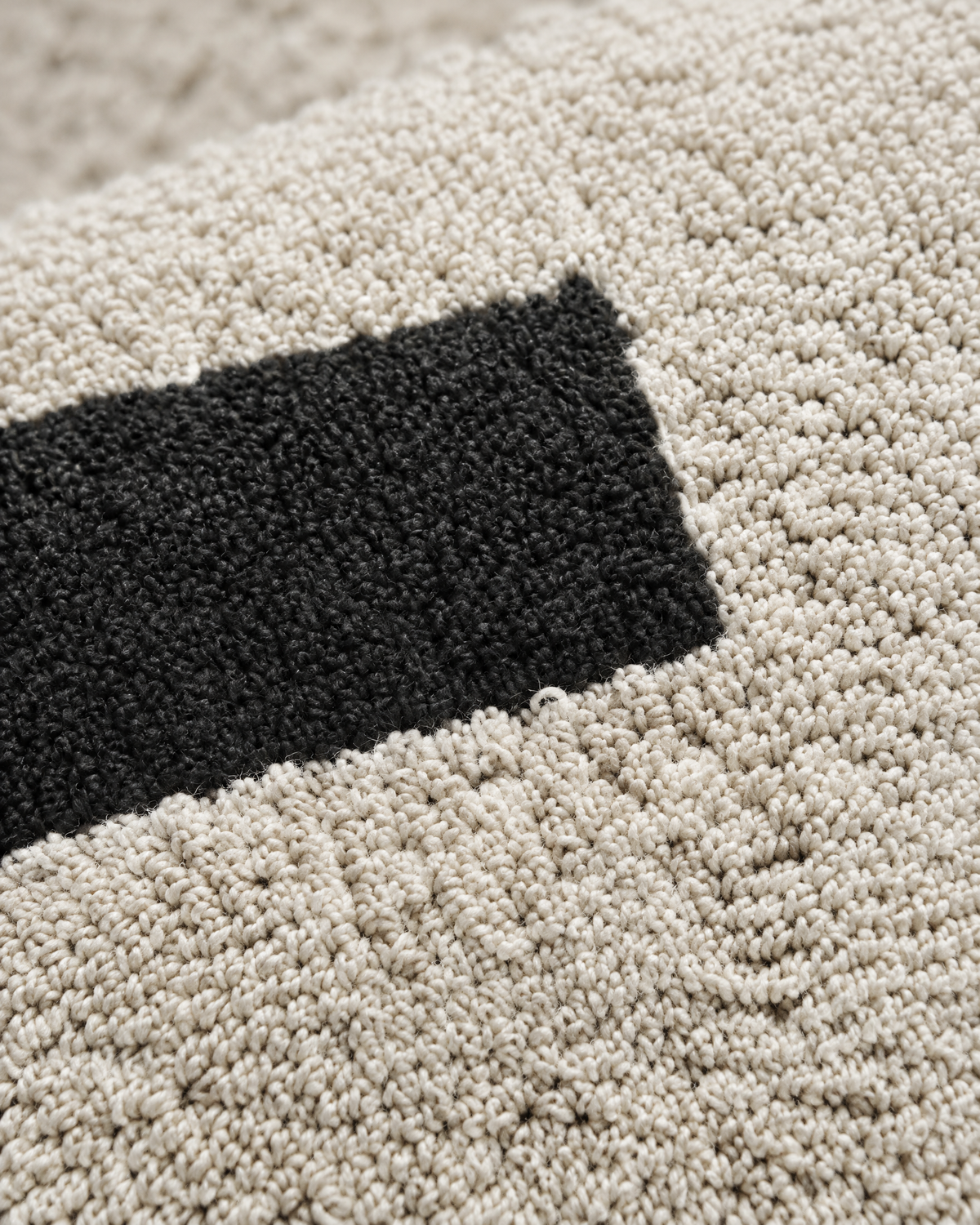 Macro close-up of ivory and black loop-pile embroidery, swirling rows of matte cotton loops meeting a solid black bar