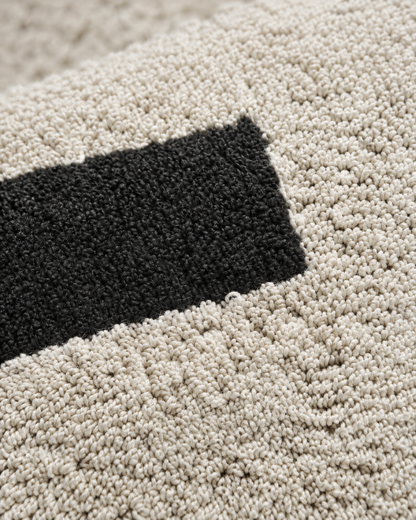 Macro close-up of ivory and black loop-pile embroidery, swirling rows of matte cotton loops meeting a solid black bar