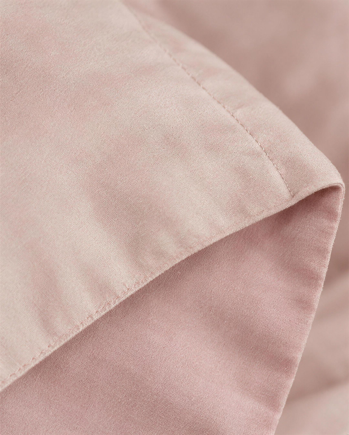Macro close-up of the blush double-face cover folded at the flange to show its two pink faces and topstitched line