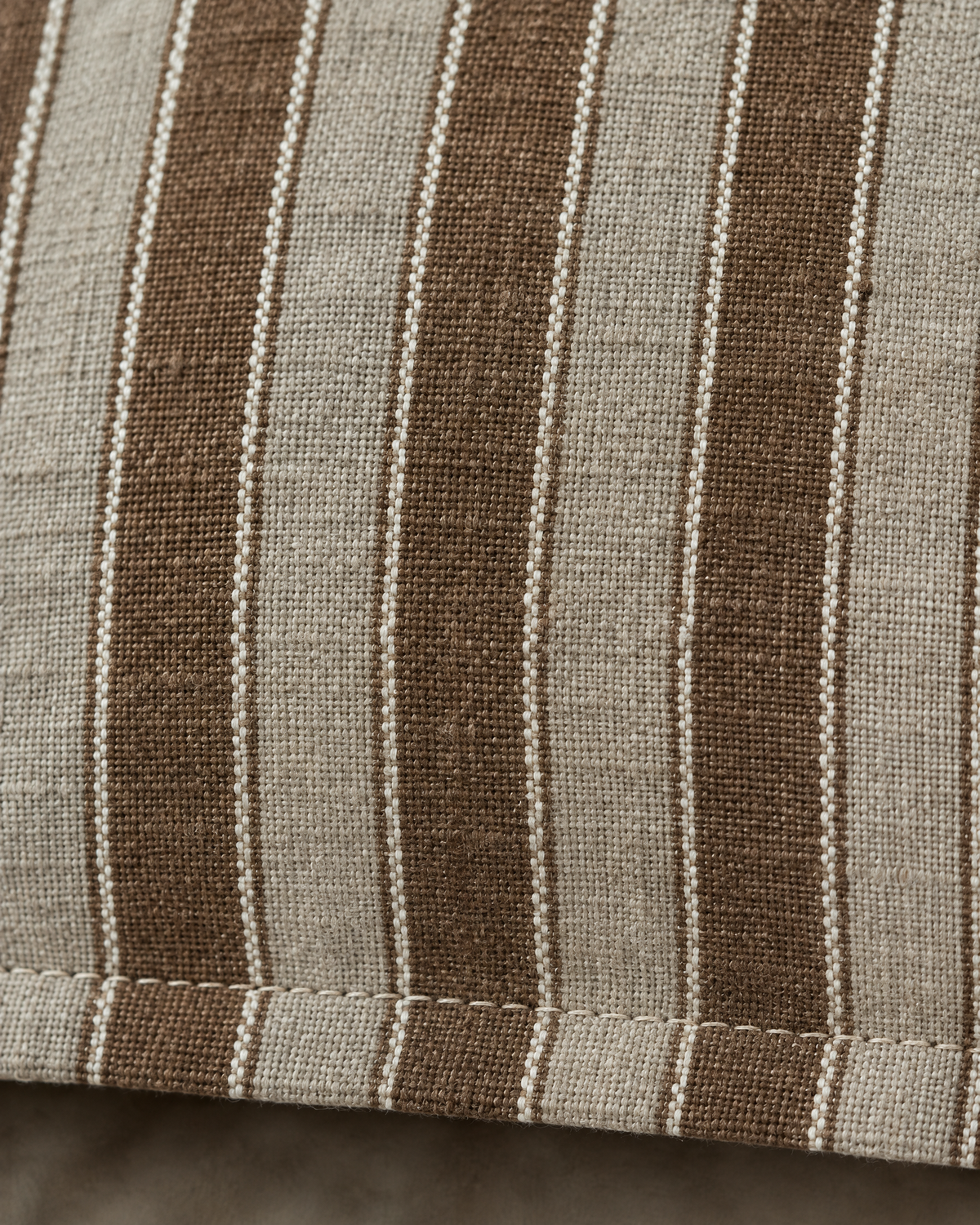 Macro close-up of Brown Stripe woven linen, cocoa and greige stripes with slubbed yarns above the topstitched flange