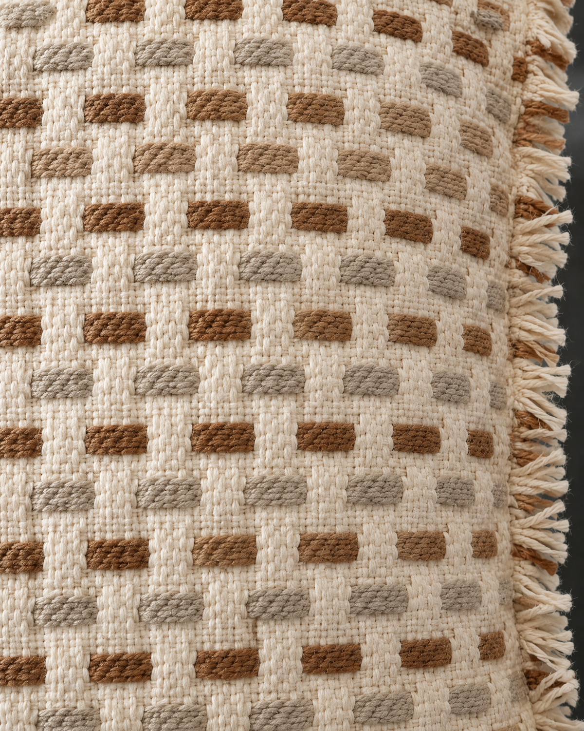 Macro close-up of rows of raised caramel, tan and greige dashes on a cream basket weave with a frayed self-fringe