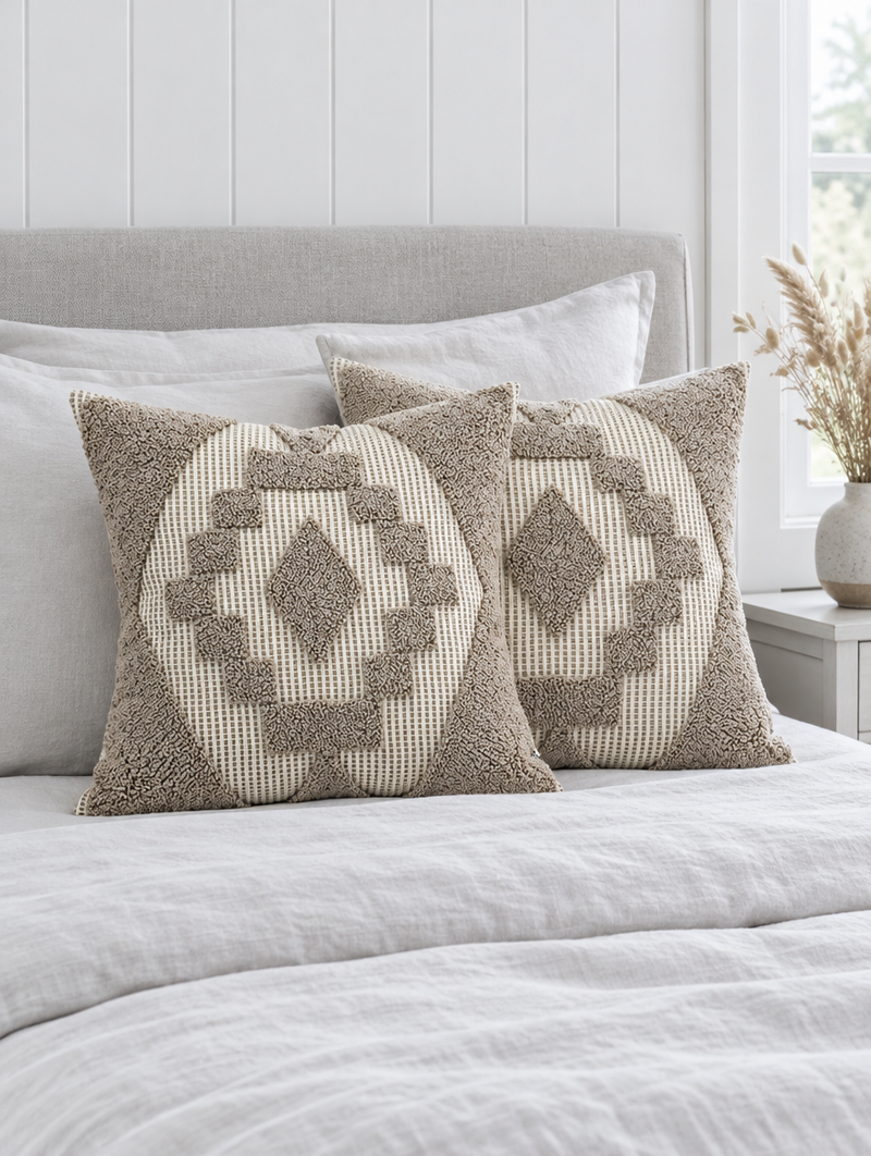 Oat and ivory loop-pile medallion cushions on grey-white linen bedding against a panelled wall