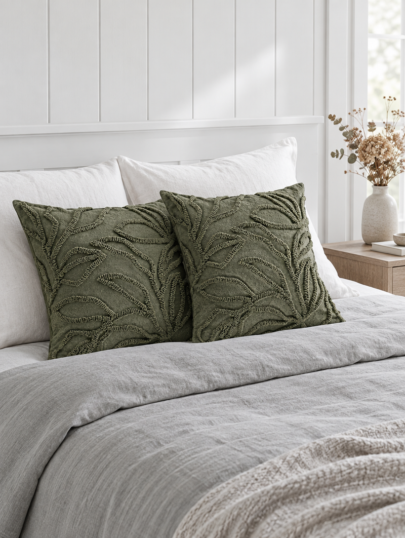 Olive green leaf-embroidered cushions on grey linen bedding with dried flowers on the nightstand