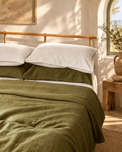 Moss green French linen sheet and pillowcases with white pillows, on a rustic wooden bed by an arched window