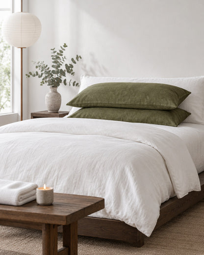 Moss green French linen pillowcases in a calm Japandi bedroom on a low dark-oak bed
