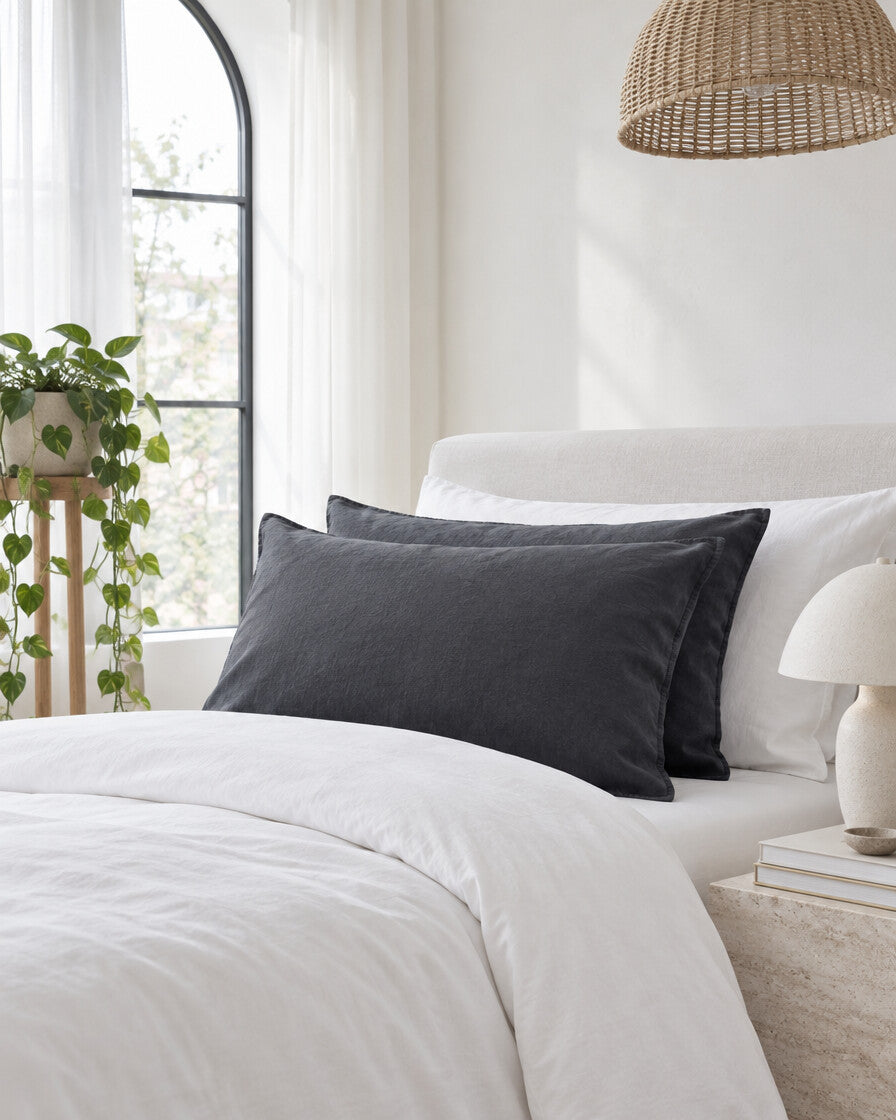 Charcoal French linen pillowcases beneath an arched window with a trailing pothos and rattan pendant