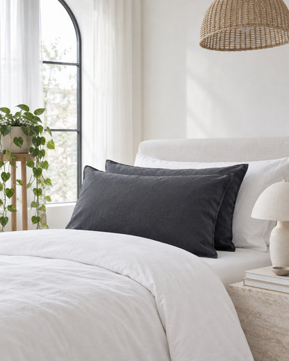 Charcoal French linen pillowcases beneath an arched window with a trailing pothos and rattan pendant