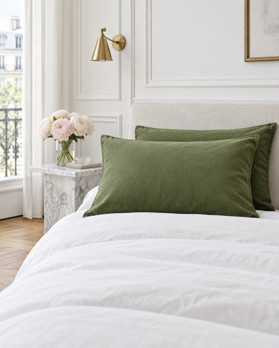 Moss green French linen pillowcases in a Parisian bedroom with panelled walls and fresh peonies