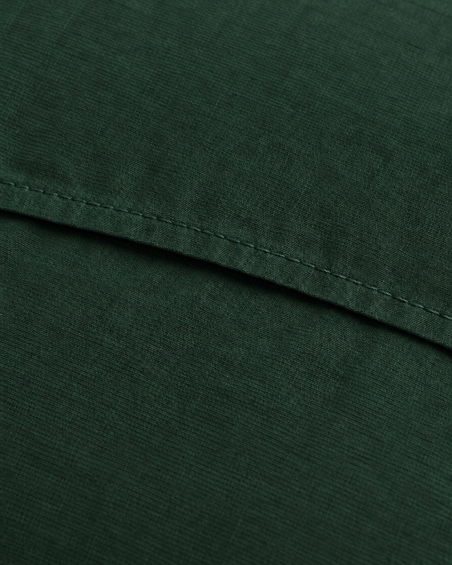 Close-up of the stitched envelope hem of a Forest Green plain cotton pillowcase in bottle green