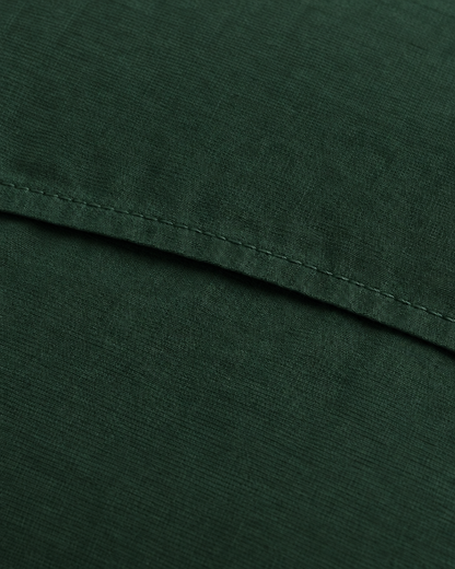 Close-up of the stitched envelope hem of a Forest Green plain cotton pillowcase in bottle green