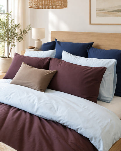 Navy, burgundy, taupe and grey plain cotton pillows stacked, styled in a bright modern townhouse bedroom