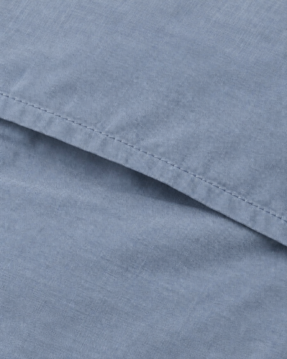 Close-up of the stitched envelope hem of a Light Jeans plain cotton pillowcase in greyed denim blue