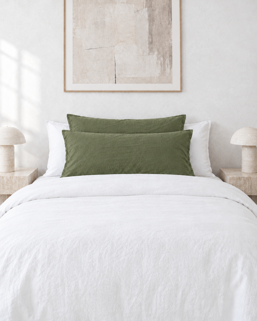 Olive plain cotton pillowcases on pillows against a white bed between bedside lamps.